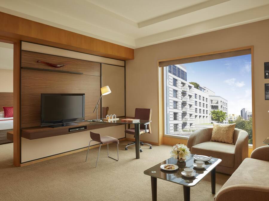 A modern hotel room with a large TV, comfortable seating, a desk, and a large window with a city view.