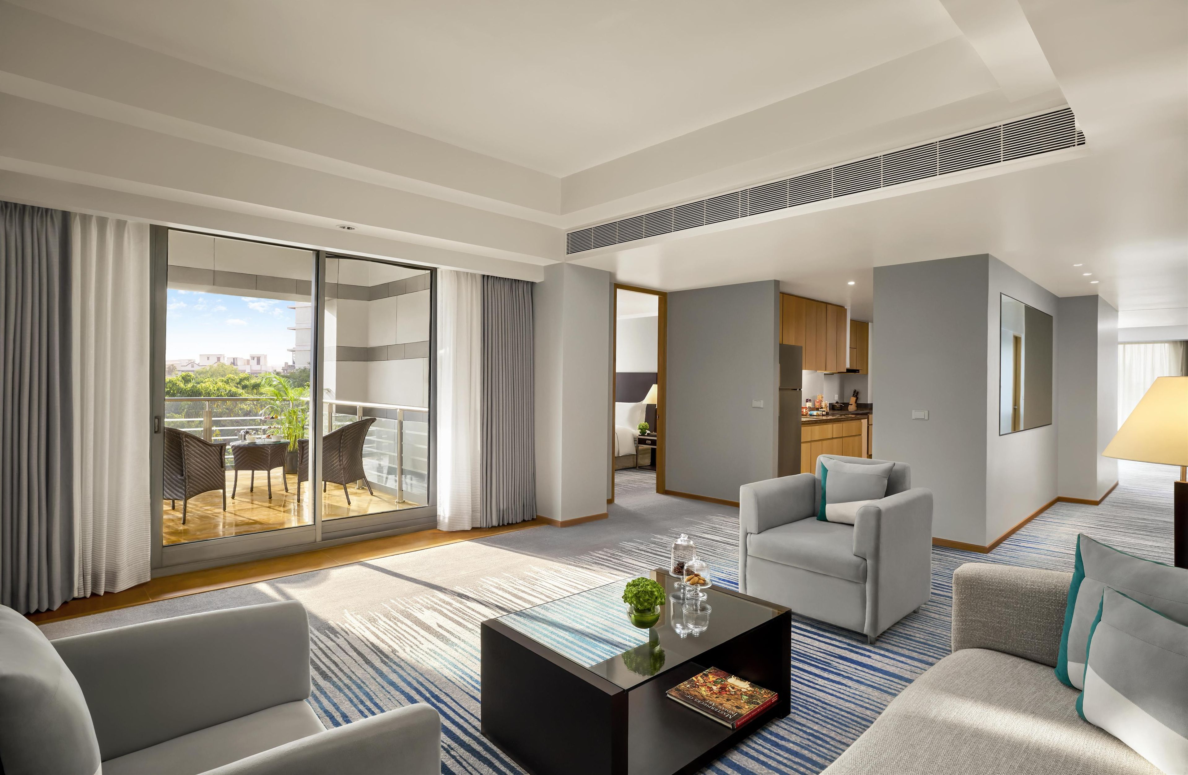 A modern hotel room with a balcony, a dining area, and a living room with a sofa and coffee table.