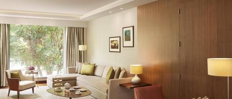 A modern hotel room with a sofa, armchairs, a coffee table, and a dining table.