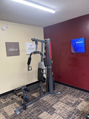 Un gimnasio con equipamiento de ejercicio, lemas motivacionales en la pared y una pantalla de televisión inspiradora.