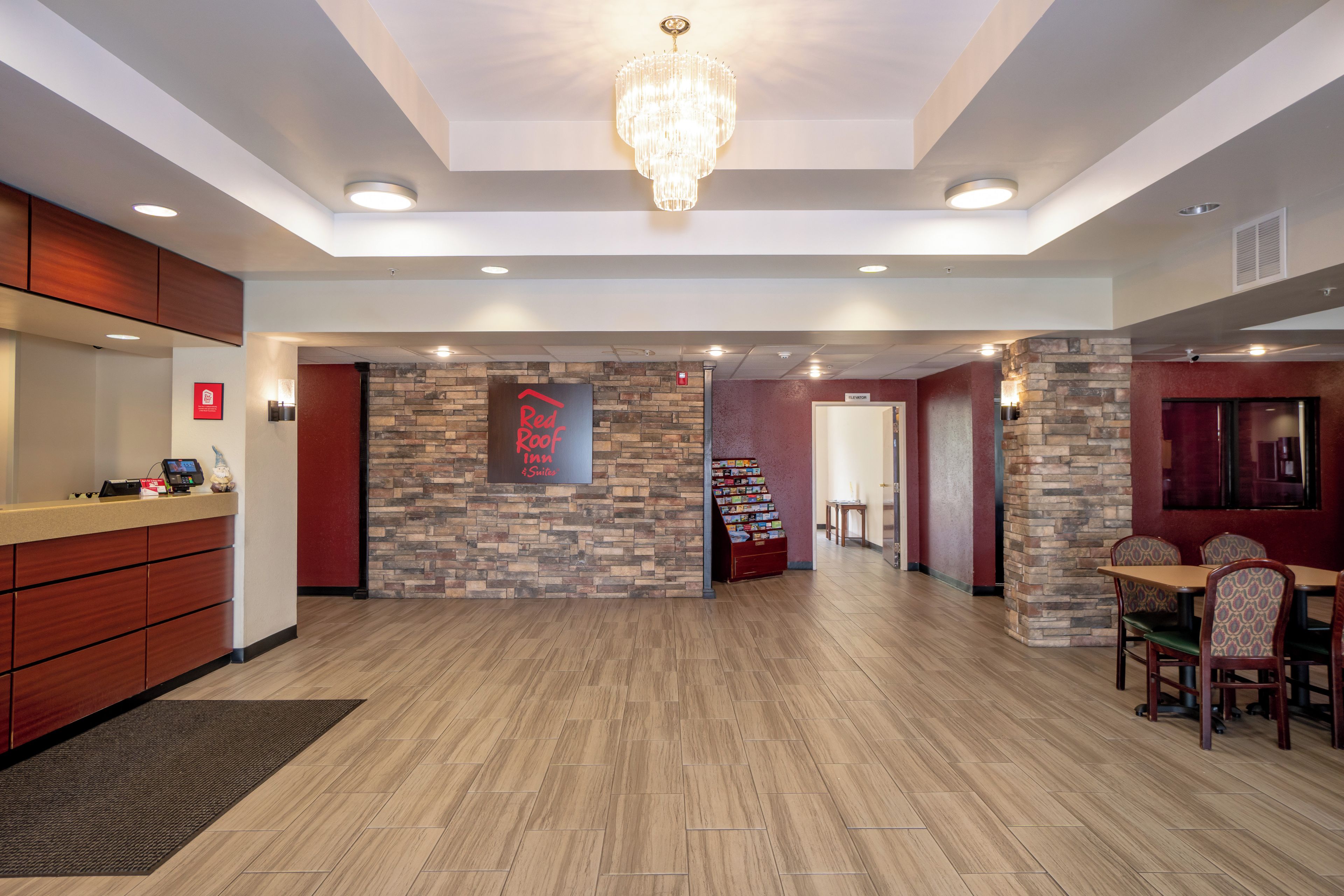 Um saguão de hotel com balcão de recepção, um candelabro, uma placa fixa na parede para Red Roof Inn & Suites e uma escada que leva ao andar superior.