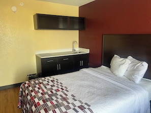 Habitación de hotel con cama, mesita de noche, lavamanos integrado y televisor de pared.