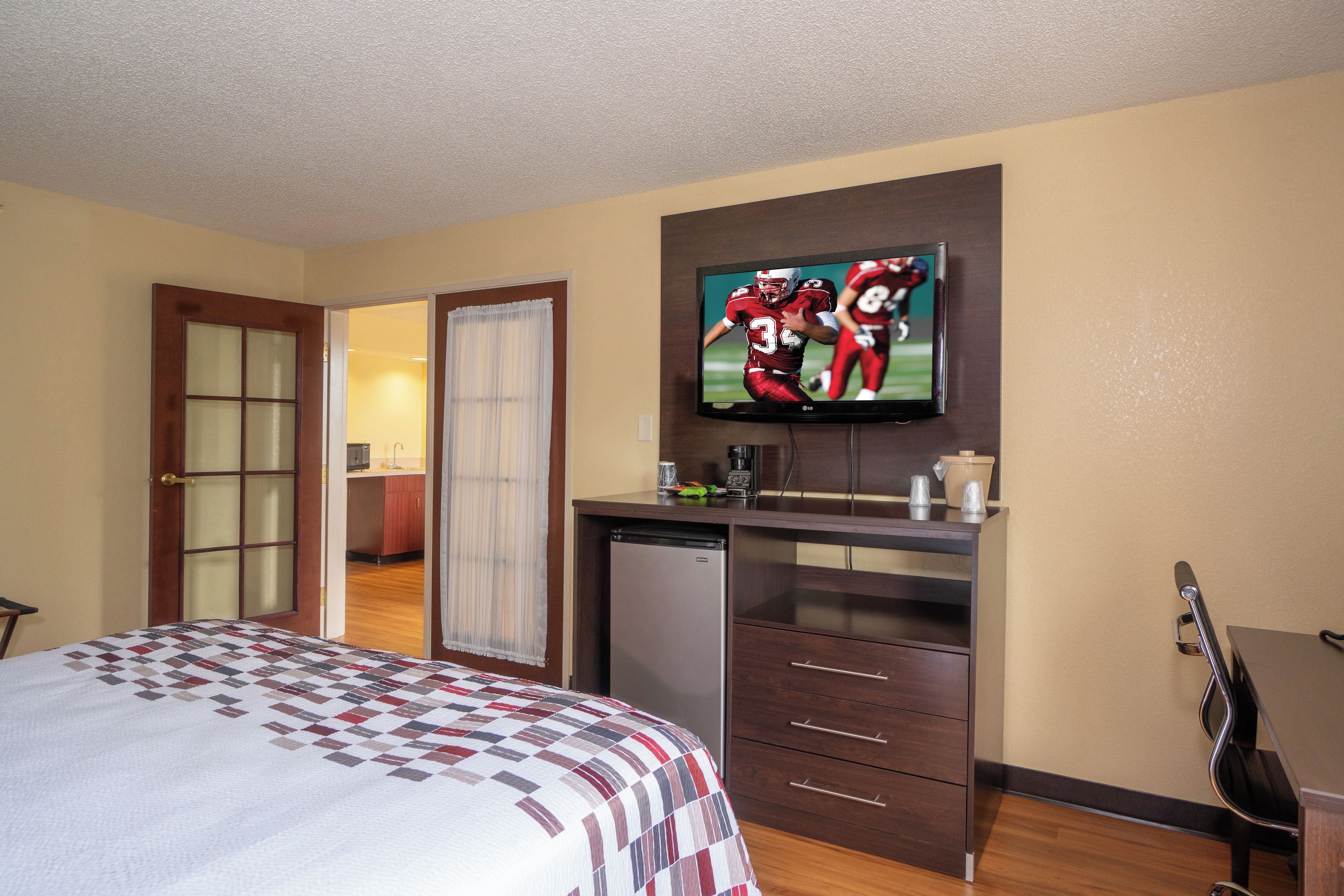 Una camera d'albergo con un letto, una scrivania, una televisione e un angolo cottura.