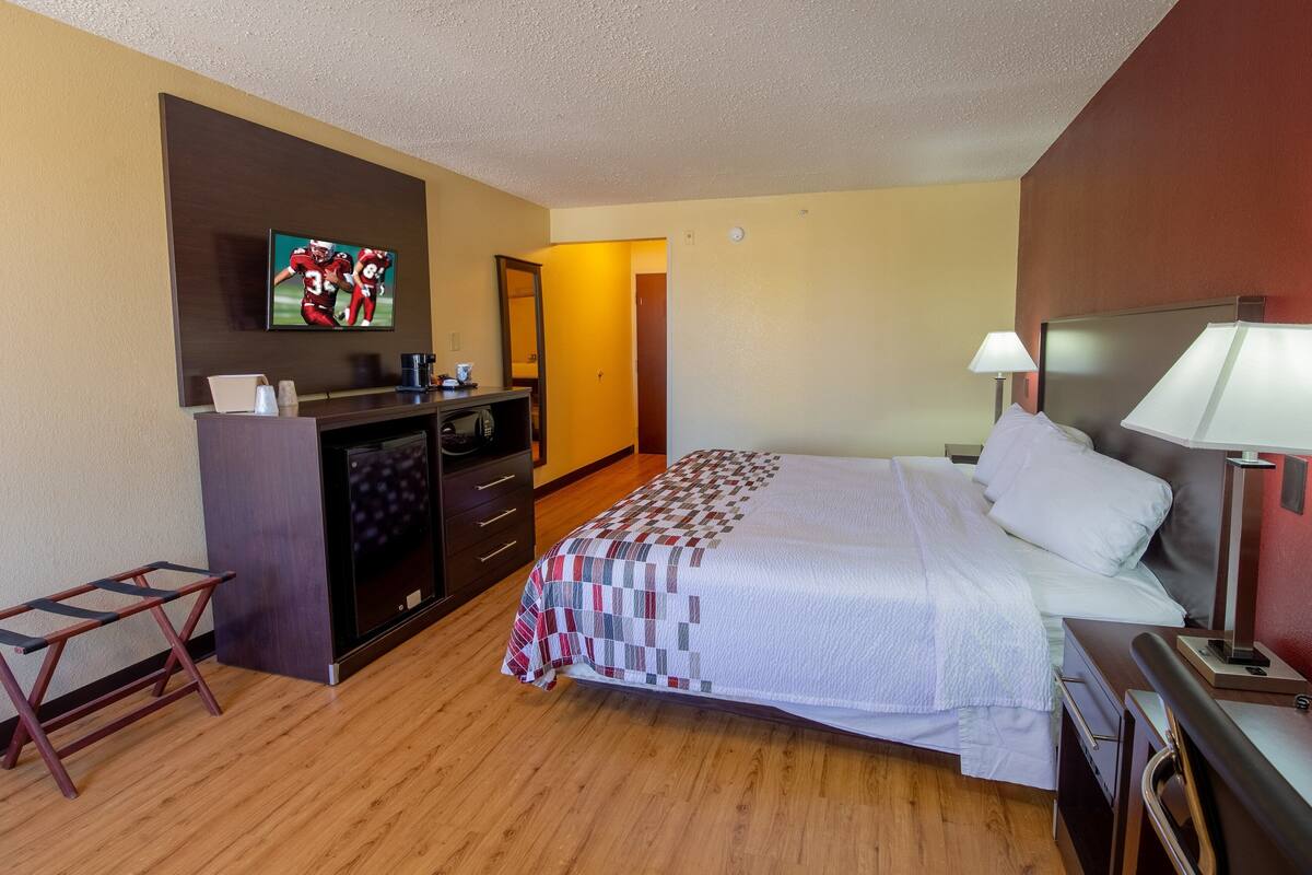 Een hotelkamer met een bed, een bureau met stoel, een televisie en een lamp.