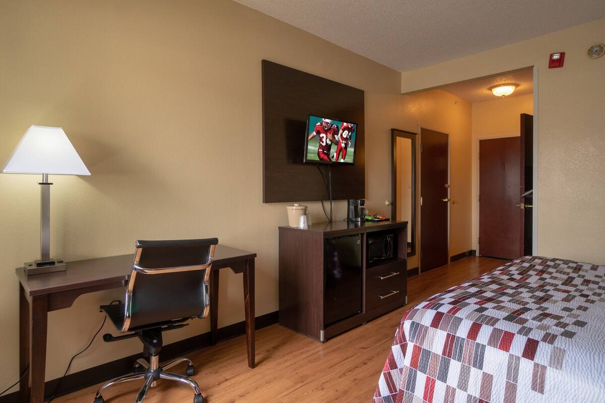 Een hotelkamer met een bureau, stoel, televisie, bed en een kleine kitchenette.