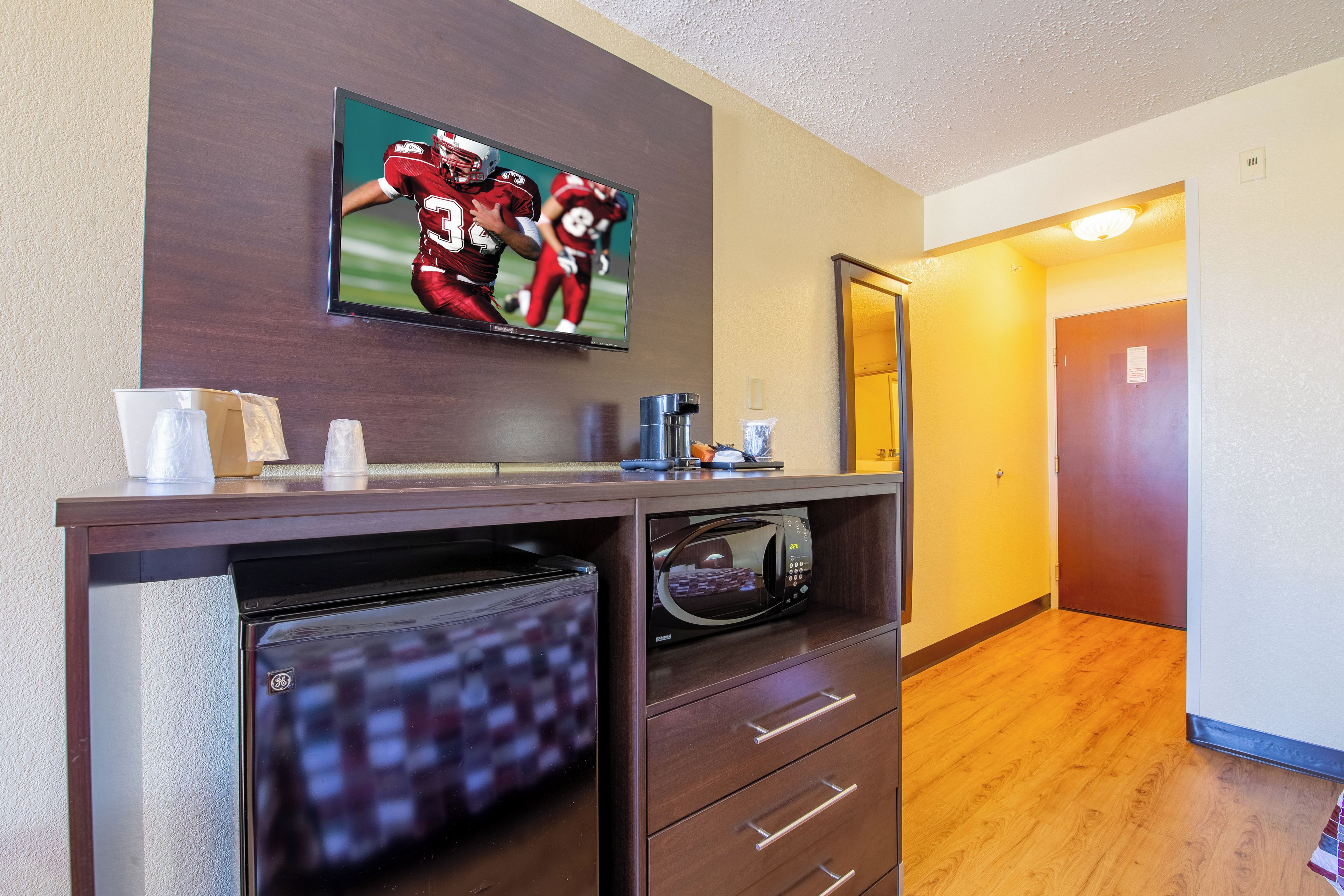 A hotel room with a flat-screen TV mounted on the wall, a microwave built into a cabinet, and a wooden floor.