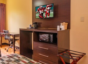 Ein Hotelzimmer mit Schreibtisch, Stuhl, Fernseher, Mikrowelle und einer kleinen Küchenzeile.