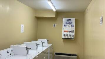 A laundry room with multiple washing machines, a sign for soap and bleach supplies, and an air conditioning unit.