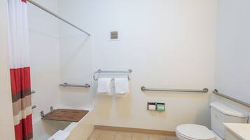 A bathroom with a toilet, a shower with a glass door, a towel rack, and a handrail.