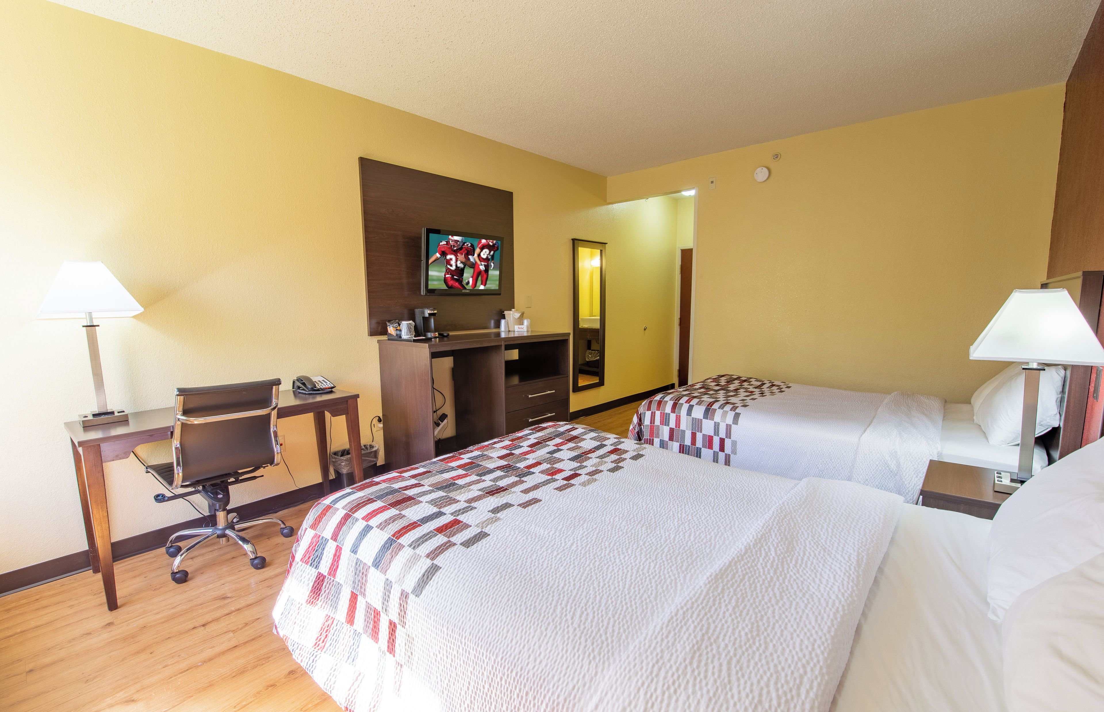 Habitación de hotel con dos camas, un escritorio, una silla, un televisor y un espejo.