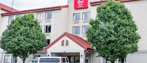 A Red Roof Inn & Suites building with a white exterior, a red roof, and two trees in front.