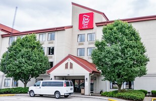 Edificio de Red Roof Inn & Suites con fachada blanca, techo rojo y dos árboles en la parte delantera.
