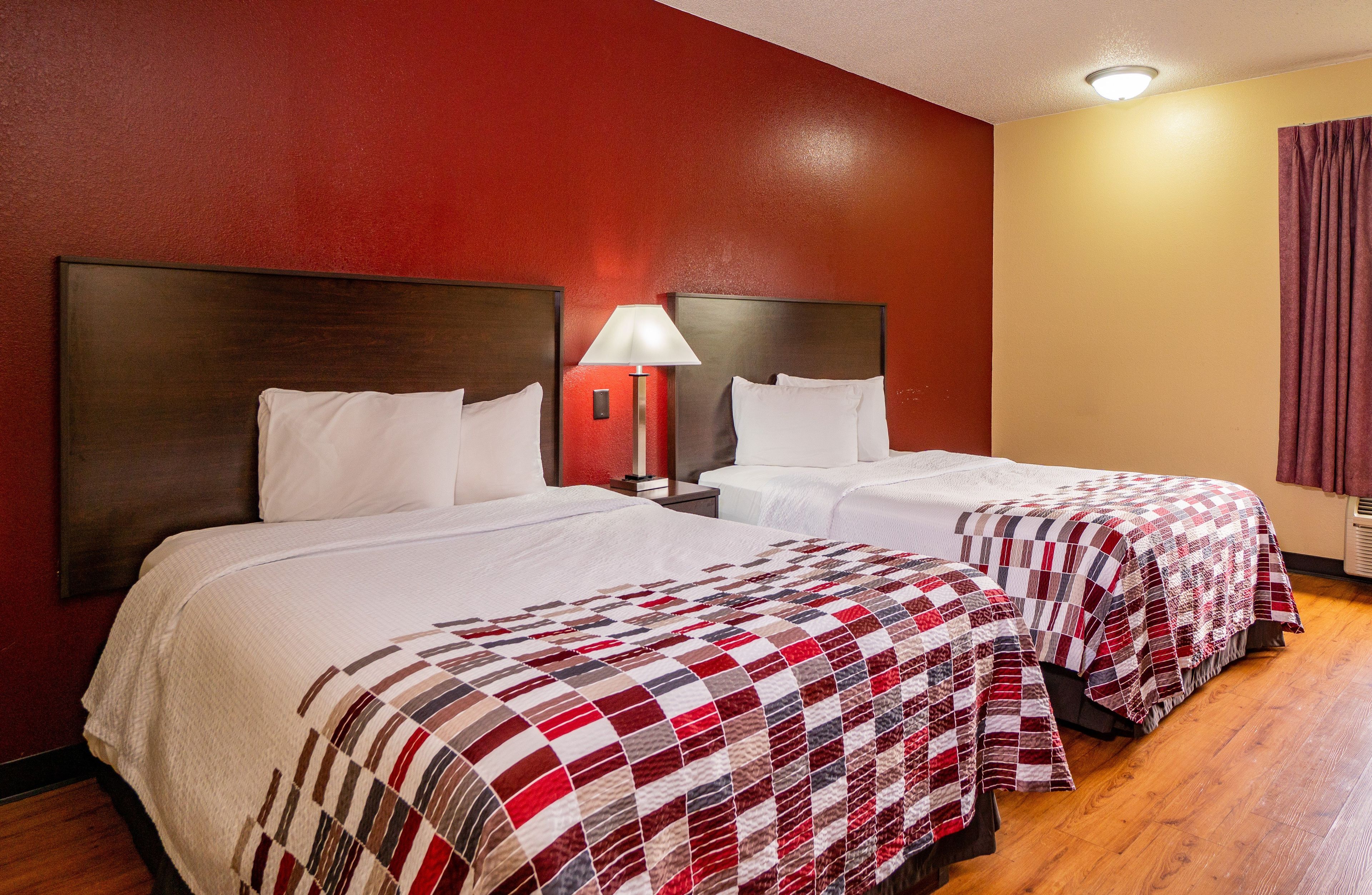 Une chambre d’hôtel avec deux lits, un mur rouge, un plancher en bois et une fenêtre avec des rideaux.