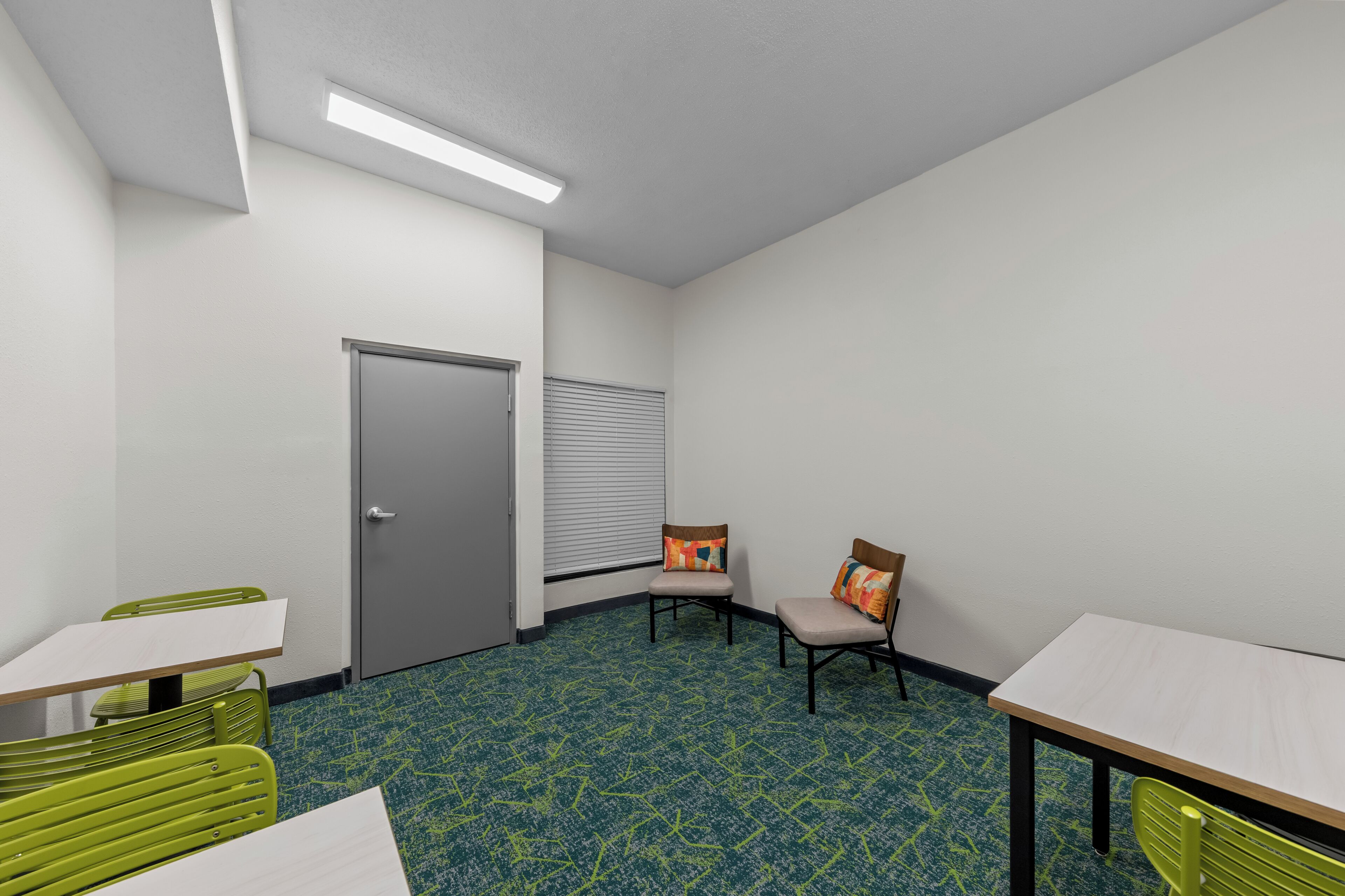Ein Zimmer mit Tür, zwei Stühlen, einem Tisch und einem gemusterten Teppich.