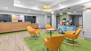 A modern hotel lobby with a reception desk, seating area with chairs, a coffee station, and a green carpet. - Spark by Hilton Cincinnati Airport South (Florence)