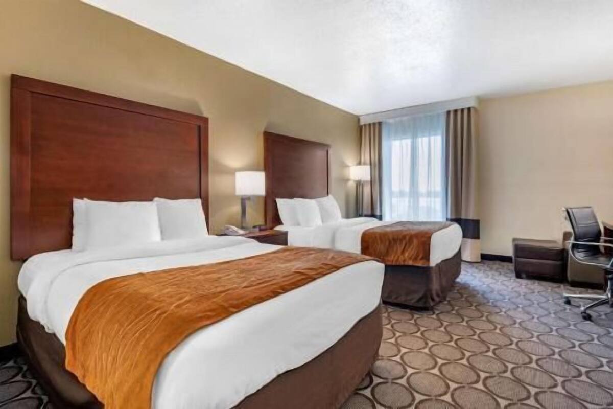 Habitación de hotel con dos camas, un escritorio, una silla y una ventana con cortinas.