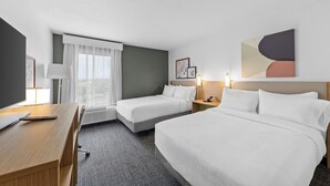 A hotel room with two beds, a desk, a lamp, a window with curtains, and a wall-mounted artwork. - Spark by Hilton Cincinnati Airport South (Florence)