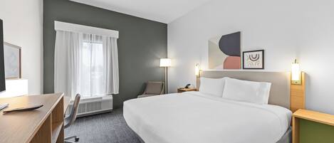 A hotel room with a large bed, a desk, a chair, a window with curtains, and wall-mounted lamps.