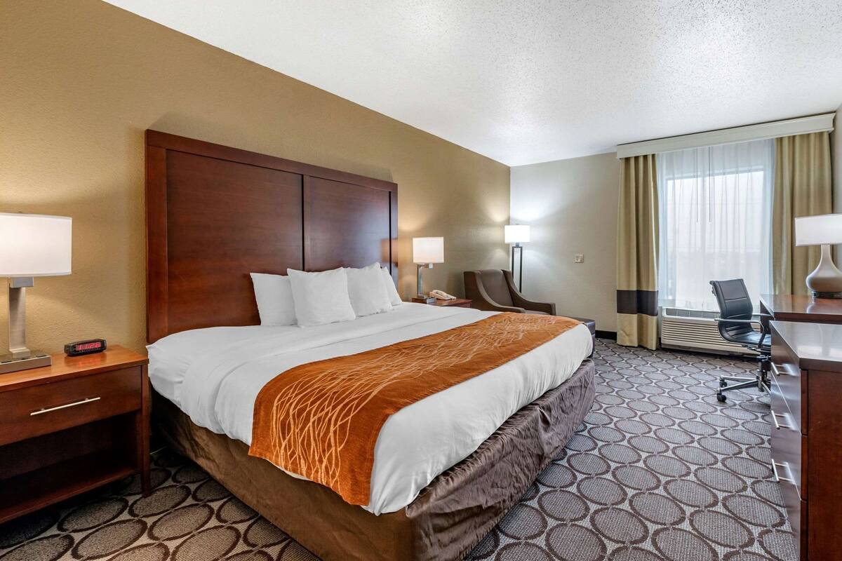 Una habitación de hotel con una cama grande, mesitas de noche, un escritorio, una silla y un ventanal con cortinas.