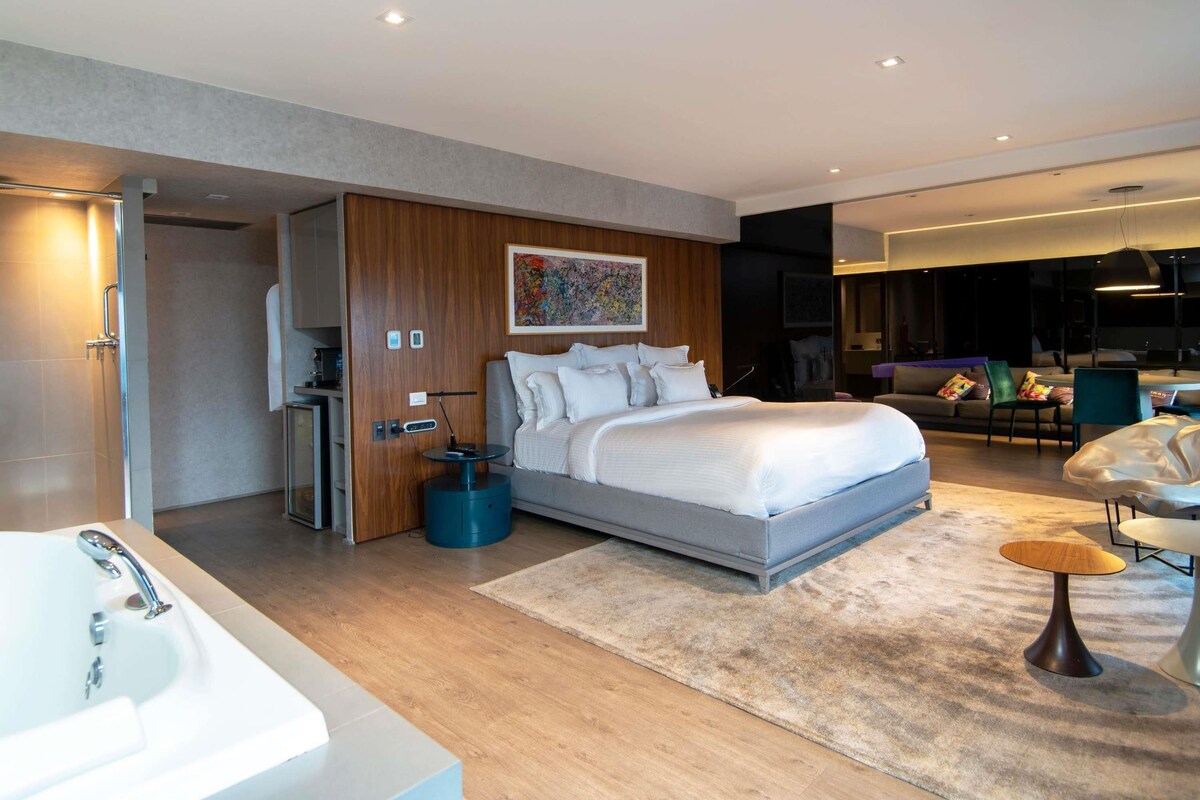 Un dormitorio moderno con una cama grande, un baño con bañera y una sala de estar con sofá y mesa de centro.