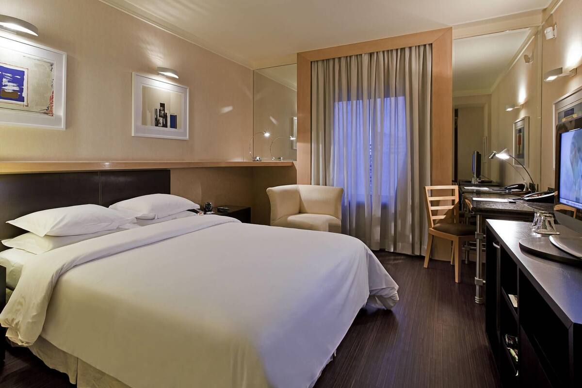 Een hotelkamer met een groot bed, een bureau met een computer, een stoel en een televisie.