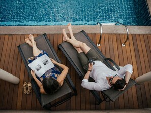 Dos sillones de exterior junto a una piscina con un muelle de madera, la piscina y una escalera de metal.