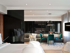 Een moderne hotelkamer met een groot bed, een bank, een zithoek met stoelen, een televisie en een grote spiegel.