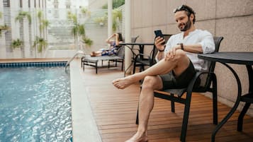 Um homem sentado à mesa junto à piscina, usando um smartphone.