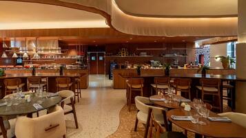 A modern restaurant with a bar area, wooden furniture, and a kitchen in the background.