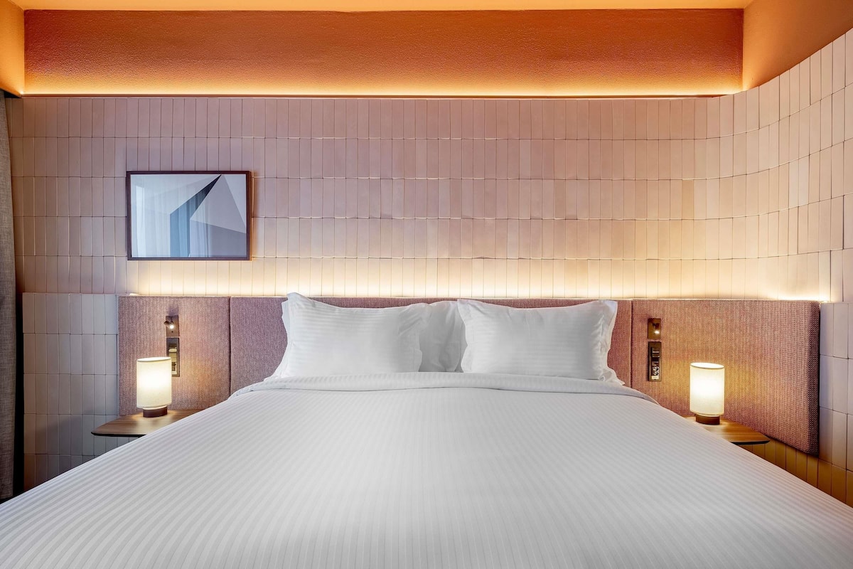 Een hotelkamer met een groot bed, twee bedlampjes, een aan de muur bevestigd schilderij en een gestructureerd plafond.