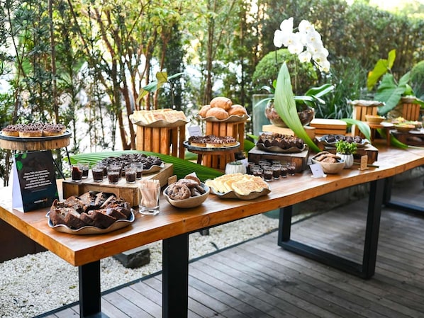 Una mesa de madera con diversos alimentos y bebidas, rodeada de follaje.