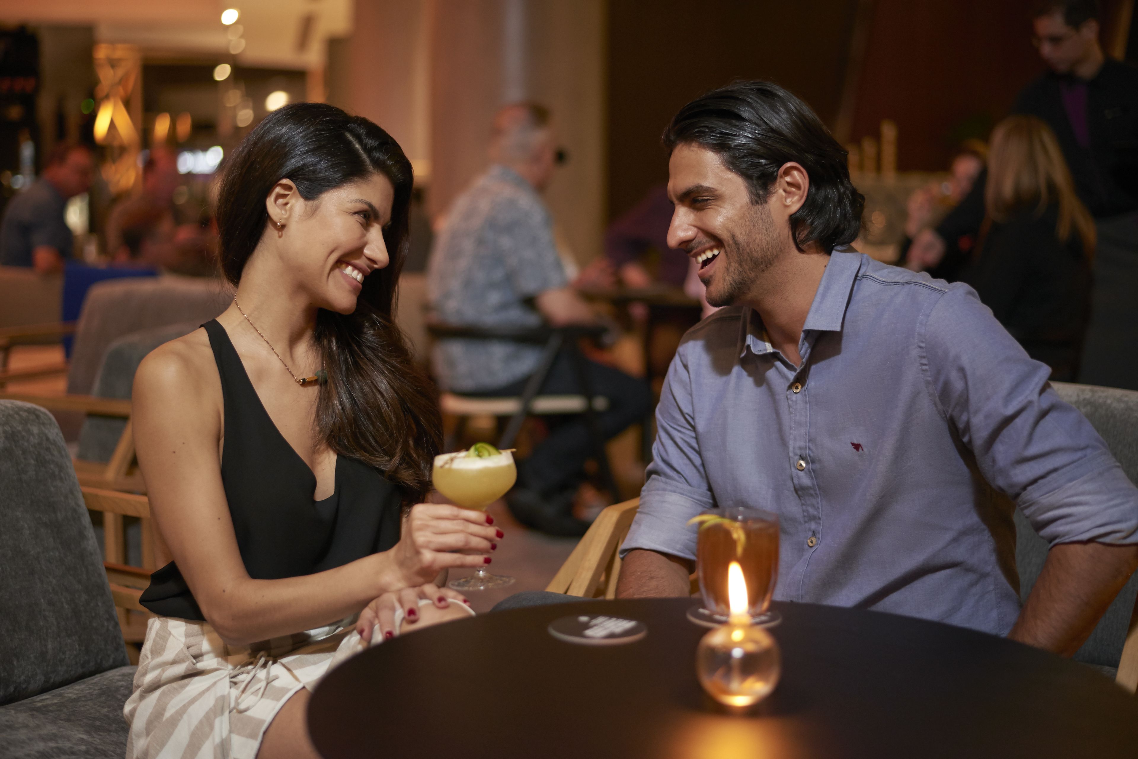 A couple seated at a round table in a restaurant with a candle on the table.