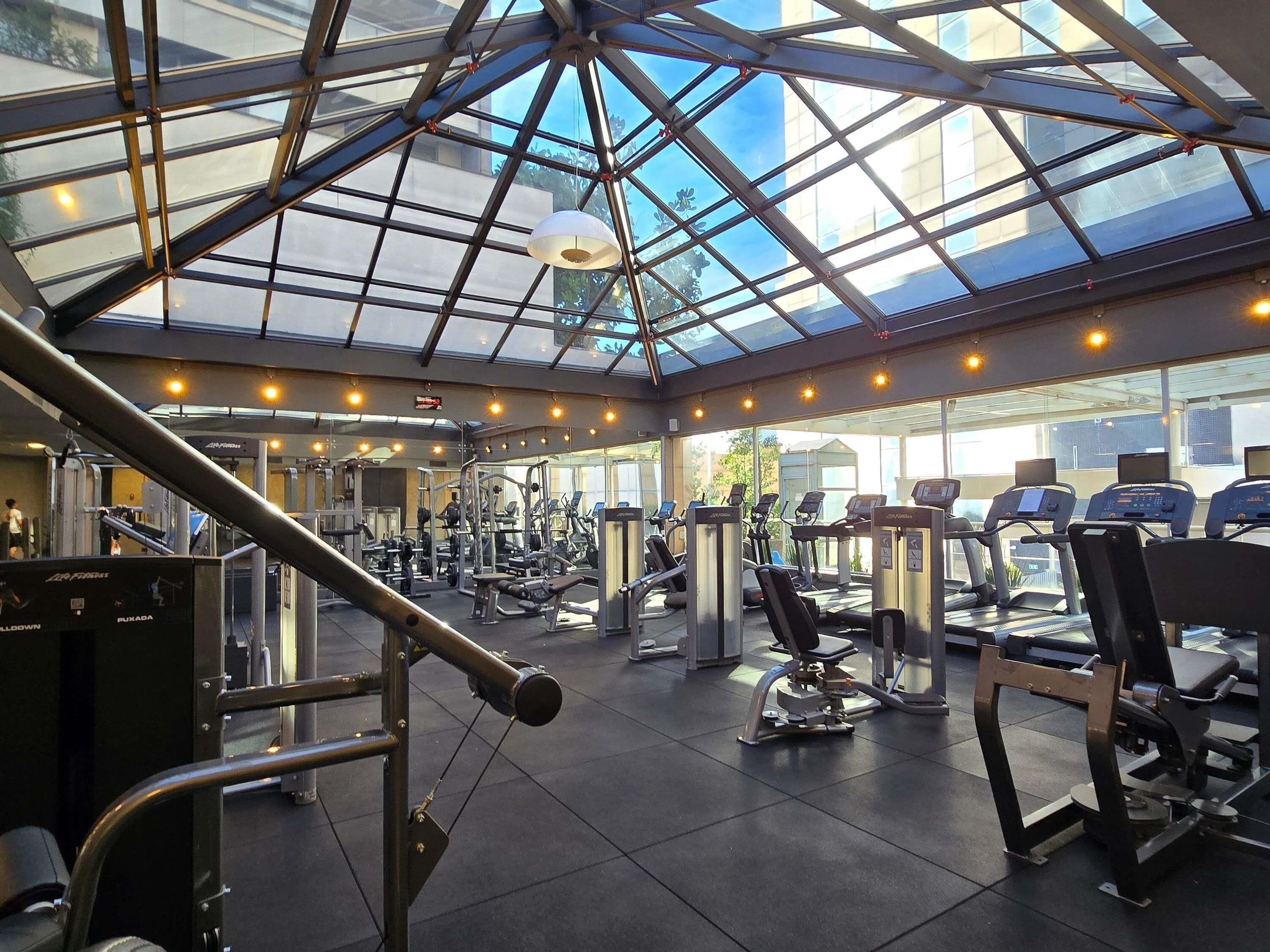 A gym with a glass ceiling, various exercise equipment, and a view of the outside.