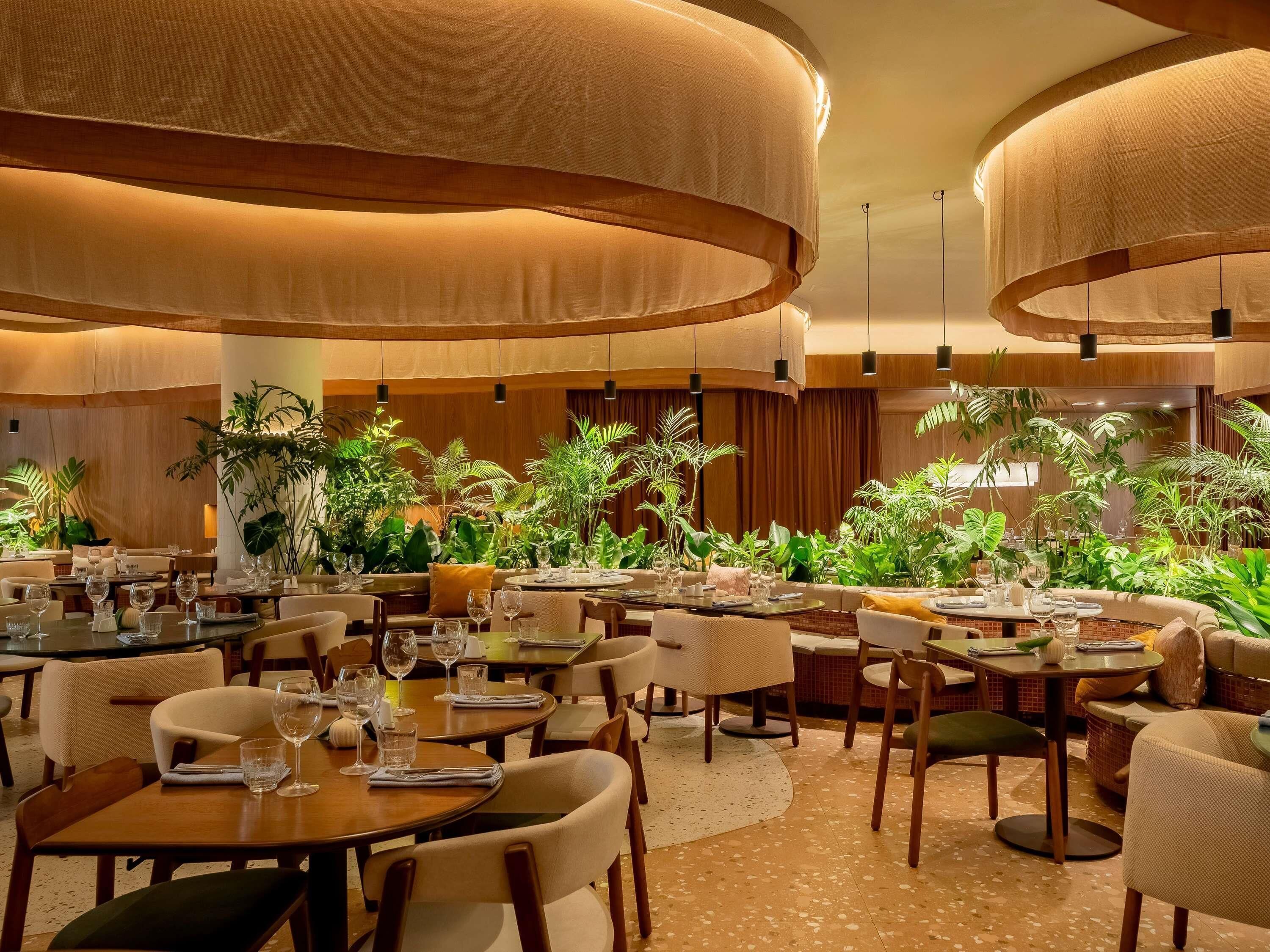 A restaurant with round tables, chairs, and hanging lamps.
