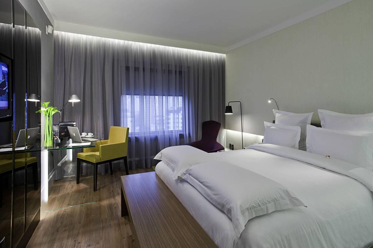 Een moderne hotelkamer met een groot bed, een bureau met twee laptops, een stoel en een televisie op een standaard.