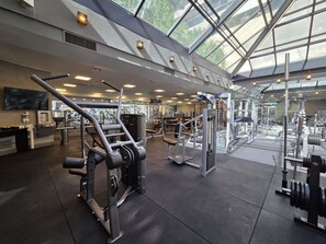 Un gimnasio con varios equipos de ejercicio, una zona de recepción y un amplio techo de cristal que deja pasar la luz natural.