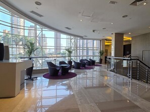 A modern lobby with a reception desk, seating area, and large windows offering city views.