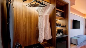 Une chambre d’hôtel dotée d’une armoire en bois, d’un peignoir, d’un téléviseur à écran plat, d’une machine à café et d’un petit coin salon.