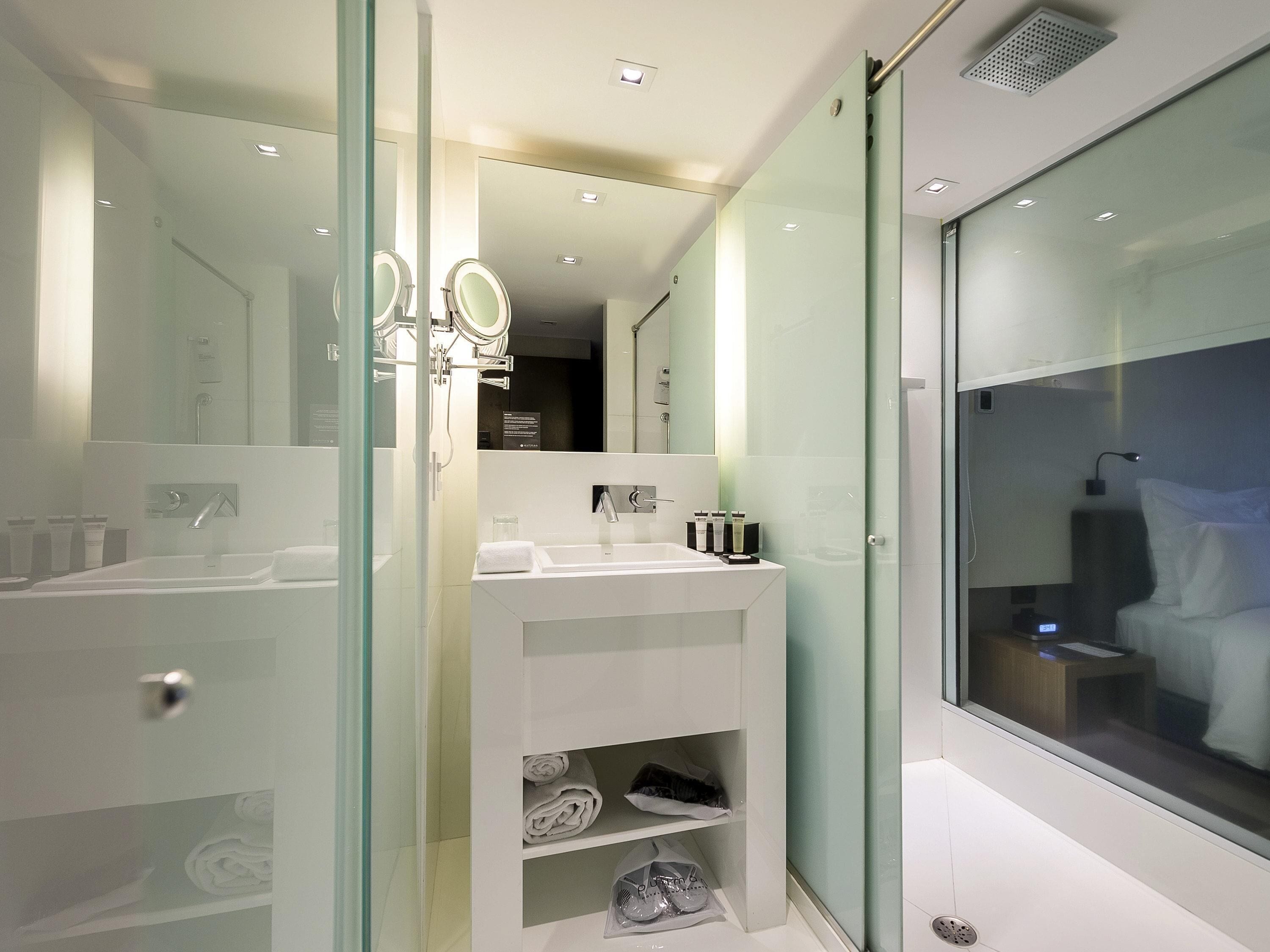 Une salle de bain moderne avec une douche à parois de verre, un lavabo blanc avec un miroir et une étagère intégrée où sont rangées les serviettes et les articles de toilette.