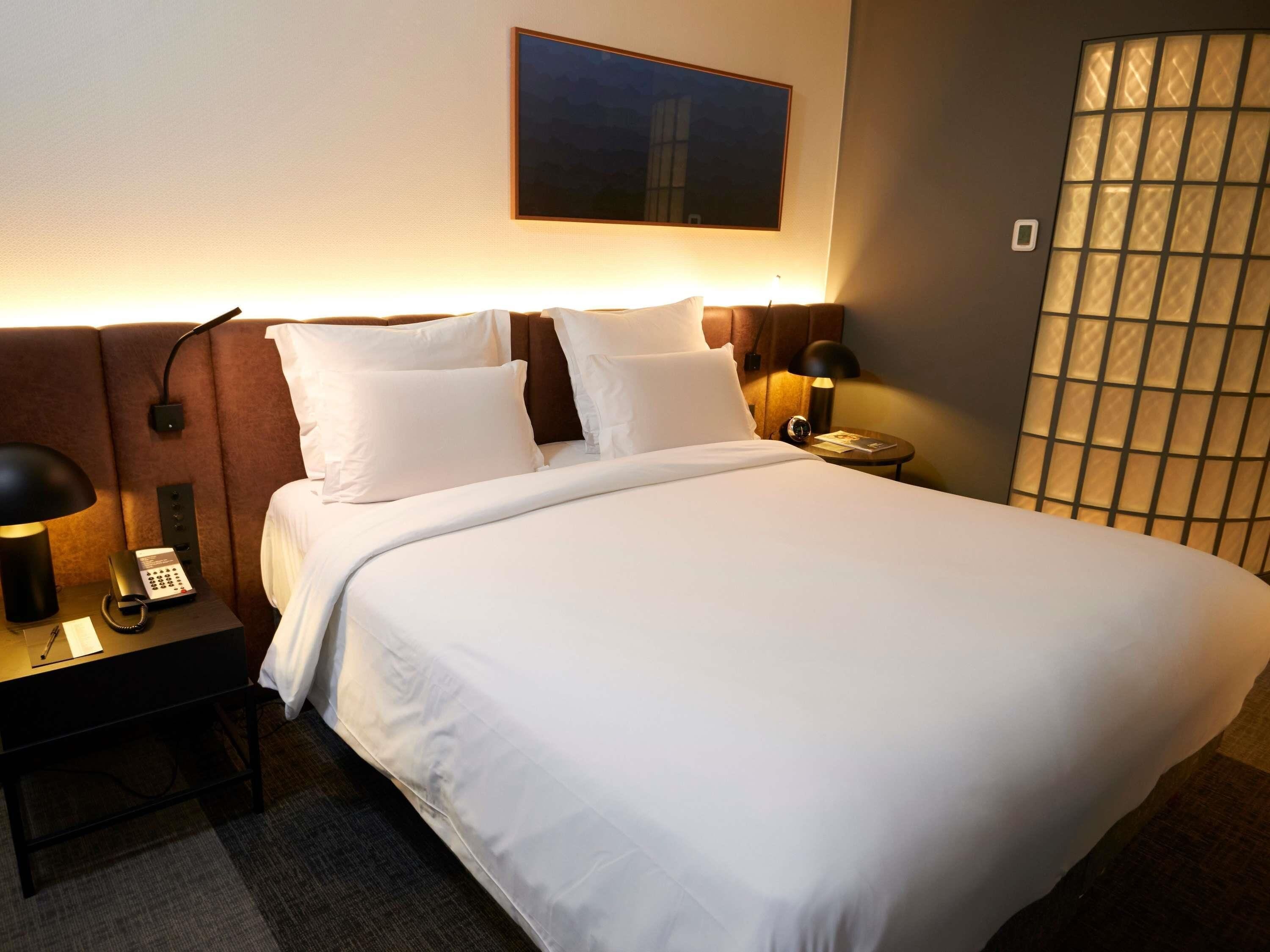 Ein Hotelzimmer mit einem Bett, Nachttischen, einem Telefon und einem an der Wand befestigten Kunstwerk.