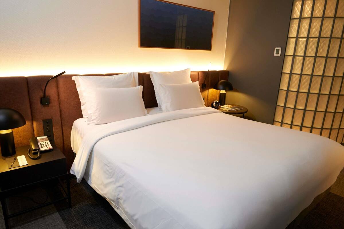 Een hotelkamer met een bed, nachtkastjes, een telefoon en een kunstwerk aan de muur.