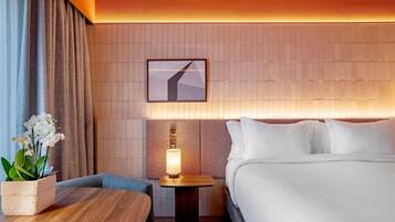 Een hotelkamer met een bed, een nachtkastje met een lamp, een klein tafeltje en een kamerplant.