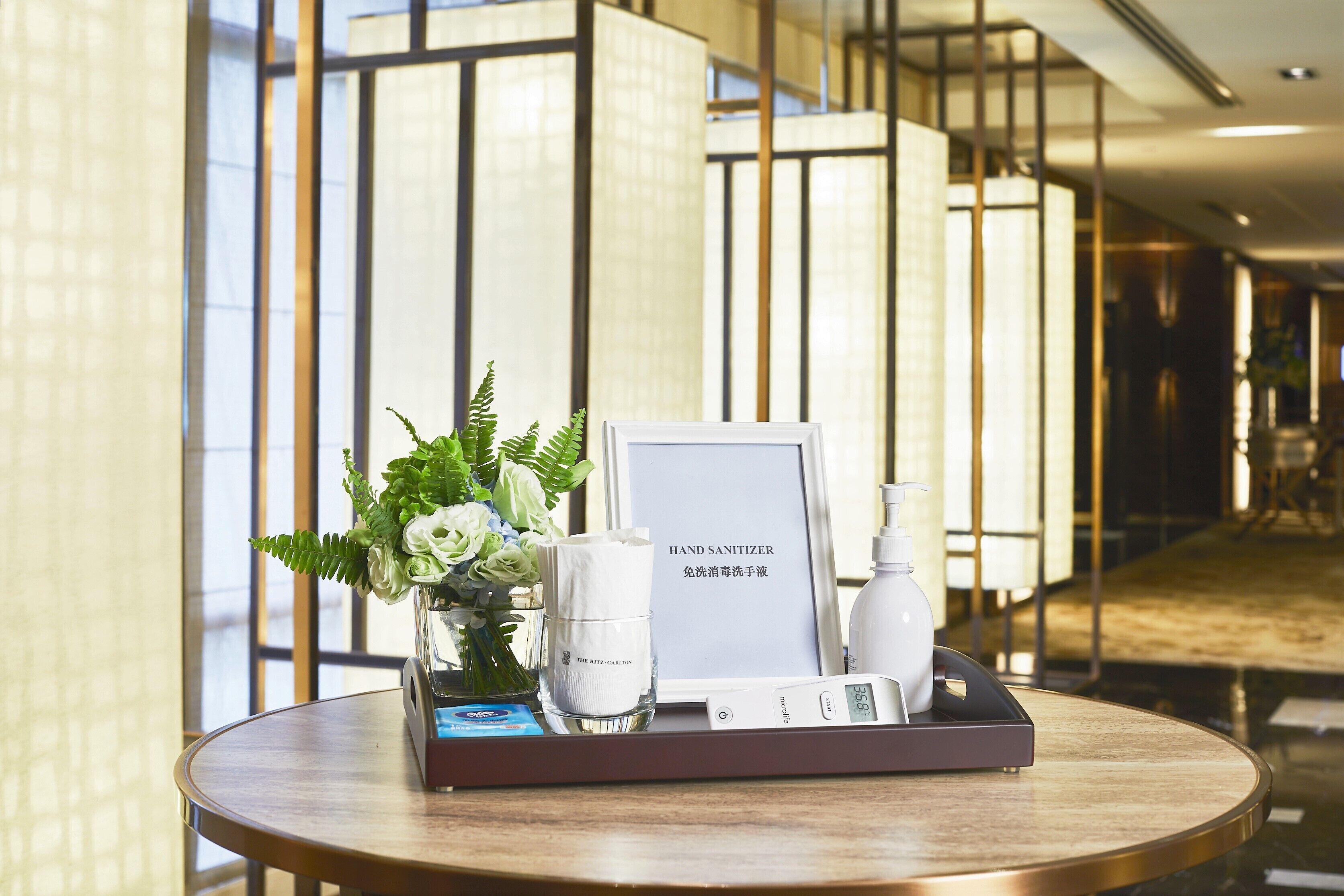 A round table with a hand sanitizer dispenser, a framed sign, a small vase with flowers, and a tissue box.