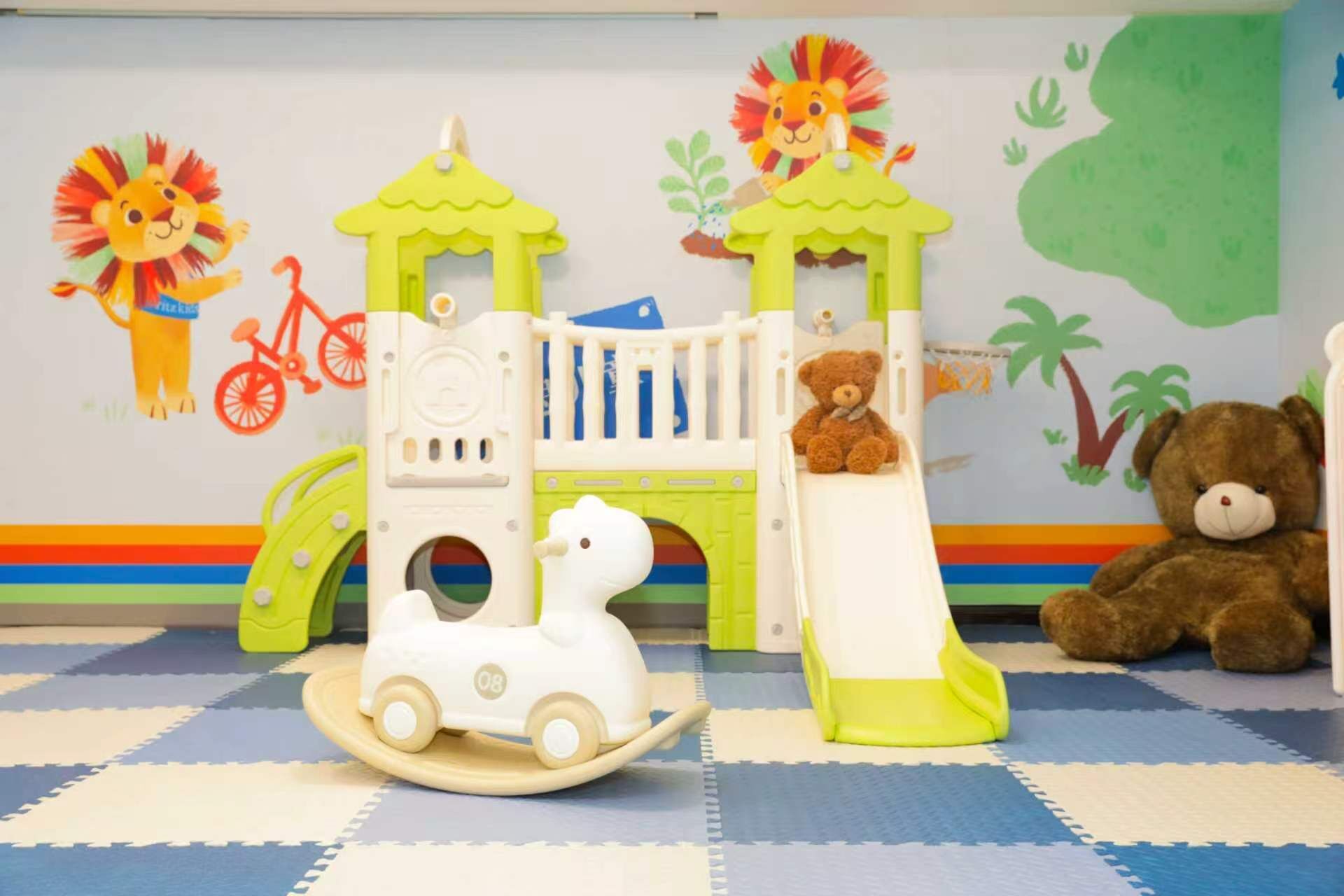 A children's play area with a slide, a small train, and a teddy bear.