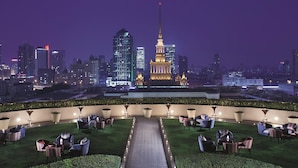 A rooftop terrace with a central pathway, surrounded by seating areas and potted plants, overlooking a cityscape with modern buildings and a prominent tower with a flag. - The Portman Ritz-Carlton, Shanghai (Shanghai)