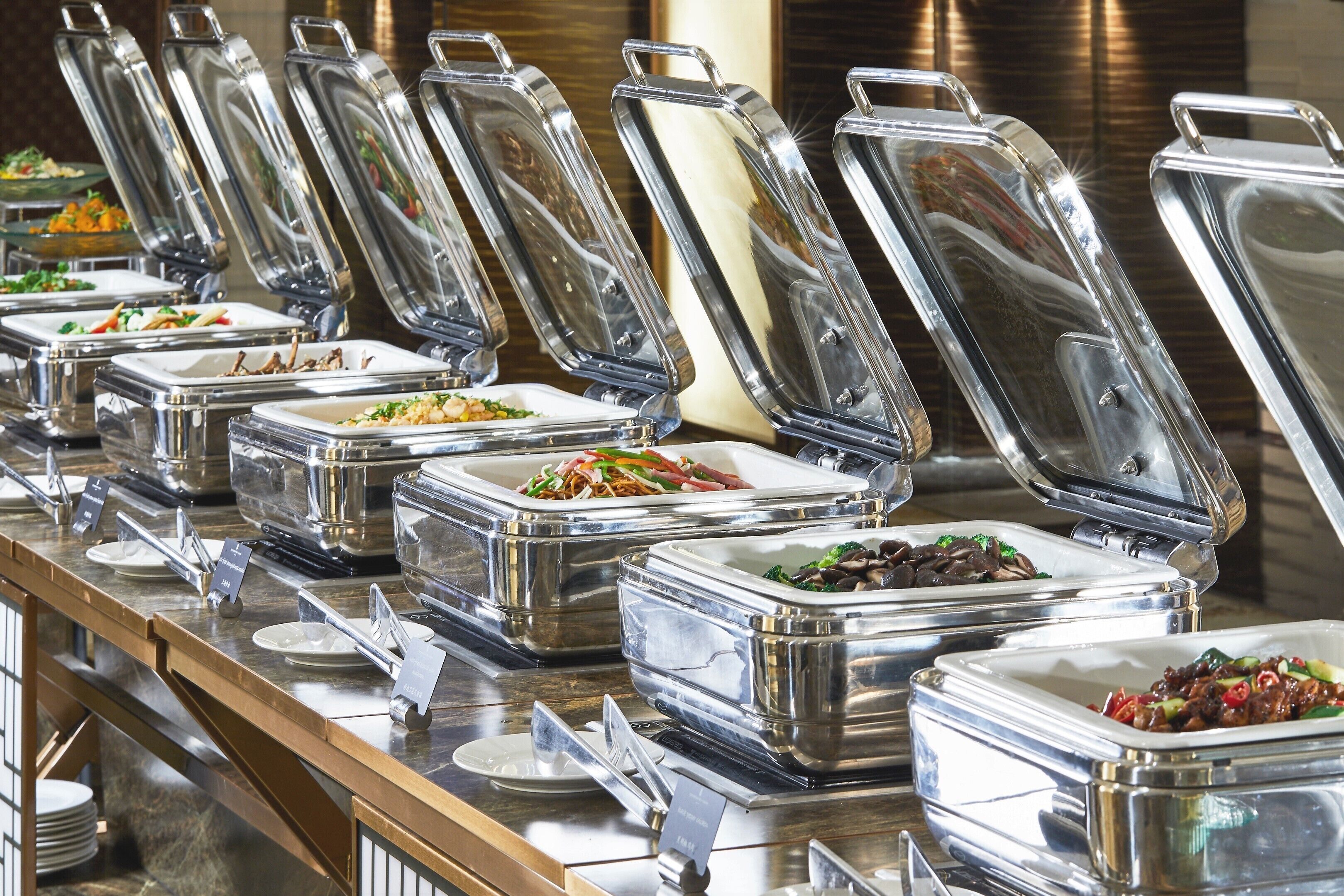 Un buffet avec de nombreux récipients contenant différents plats, chacun étant doté d’un couvercle transparent et d’une étiquette.
