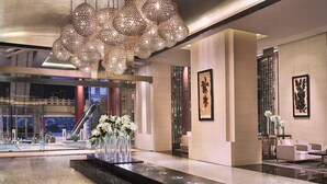 Una hall moderna con un grande lampadario, una reception con vasi di fiori e un'area salotto con divani.