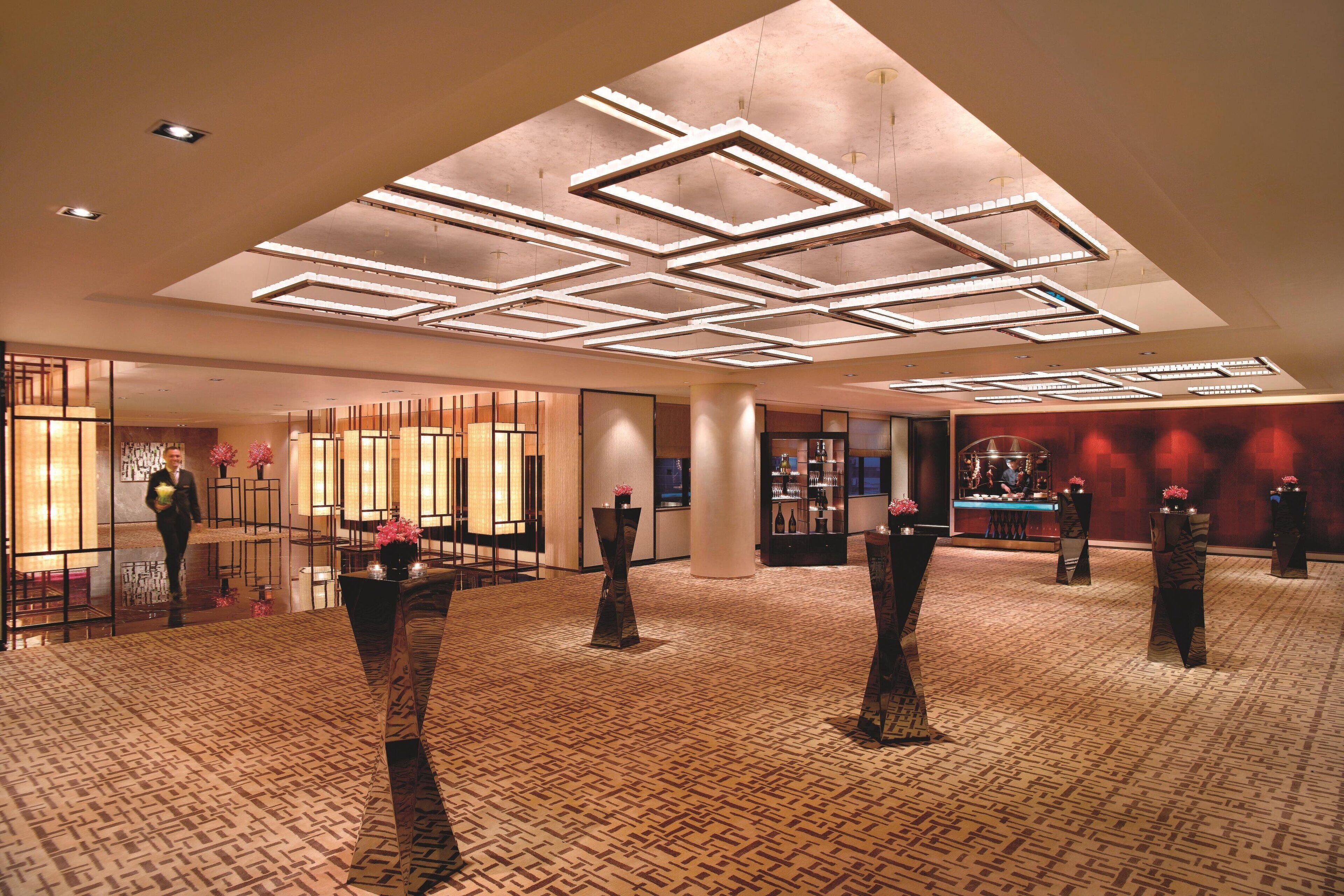 A spacious lobby with a geometric ceiling design, a patterned carpet, and several tall, dark columns with vases.
