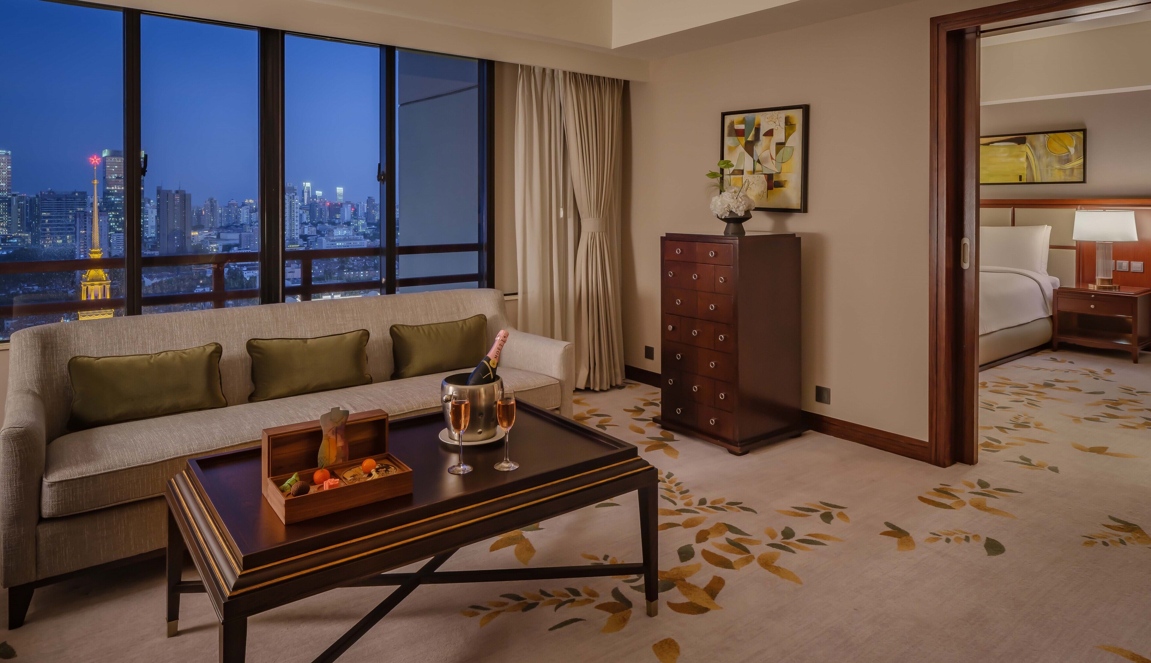 Une chambre d’hôtel avec un canapé, une petite table sur laquelle se trouvent une bouteille et des verres, une commode et un lit.