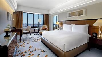Habitación de hotel con una cama grande, dos sillas, un escritorio y vistas a la ciudad.